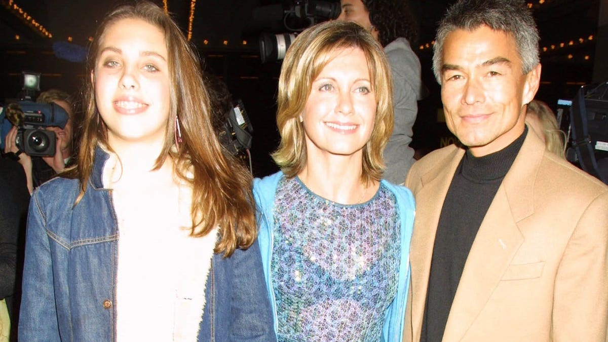 Olivia Newton John standing with daughter Chloe and Patrick Kim McDermott