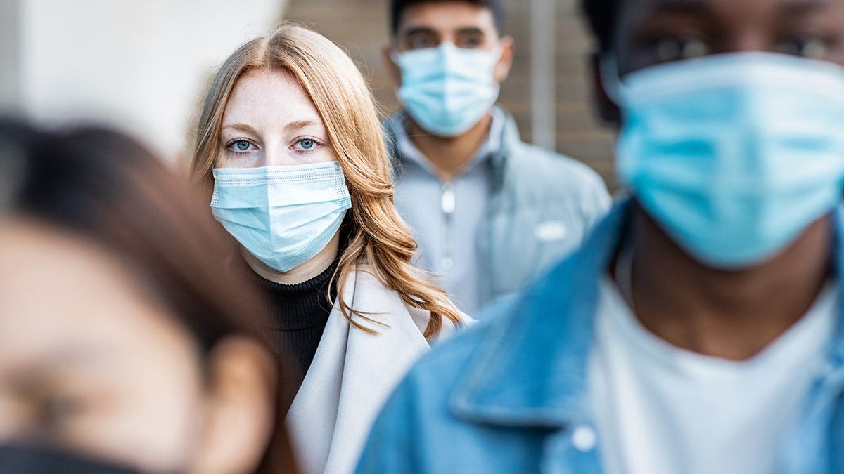 people wearing face masks walking on a city pavement.