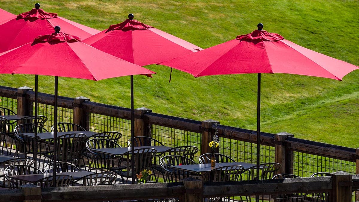 Red umbrellas shading outdoor tables on a patio with green grass