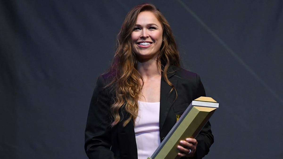 Ronda Rousey holding a trophy onstage astatine the UFC Hall of Fame induction.