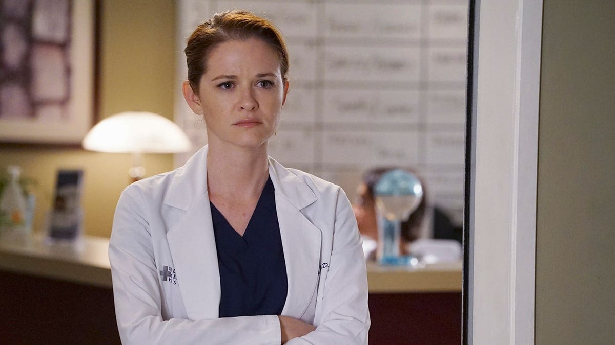 Sarah Drew standing in a hospital setting in character as April Kepner