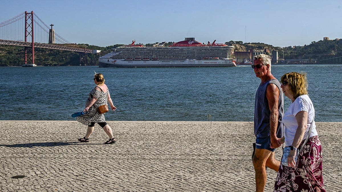 Tourists walking by the river in Belem area with Scarlet Lady cruise ship sailing on the Tagus River in Lisbon