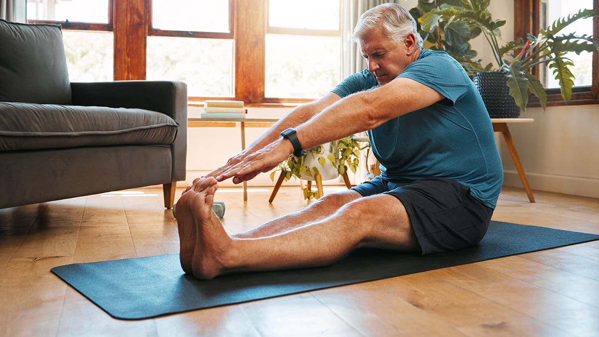 Senior man stretching on yoga mat in living room