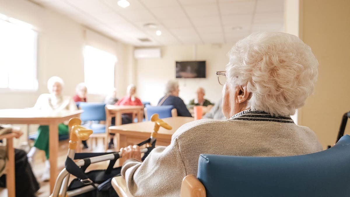 Senior woman with short white hair sitting on chair with foldable walker in nursing home