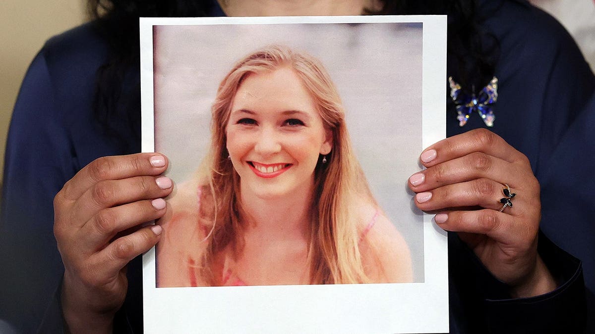 Sharlene Rochard holding a photograph of Virginia Giuffre at a news conference with Sen. Chuck Schumer in Washington, D.C.