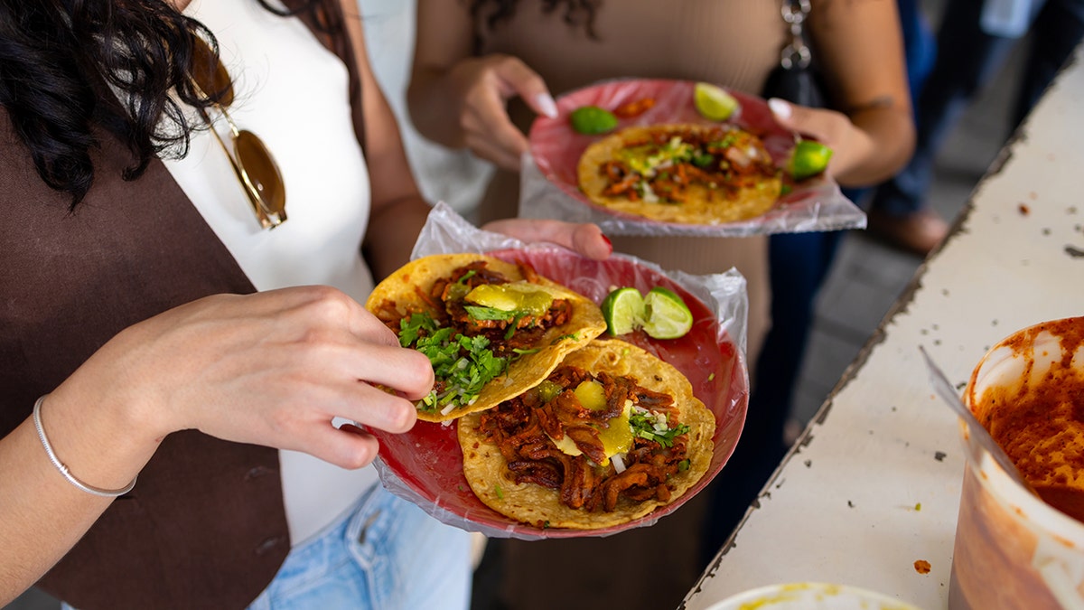 Two women eat tacos al pastor on plates.