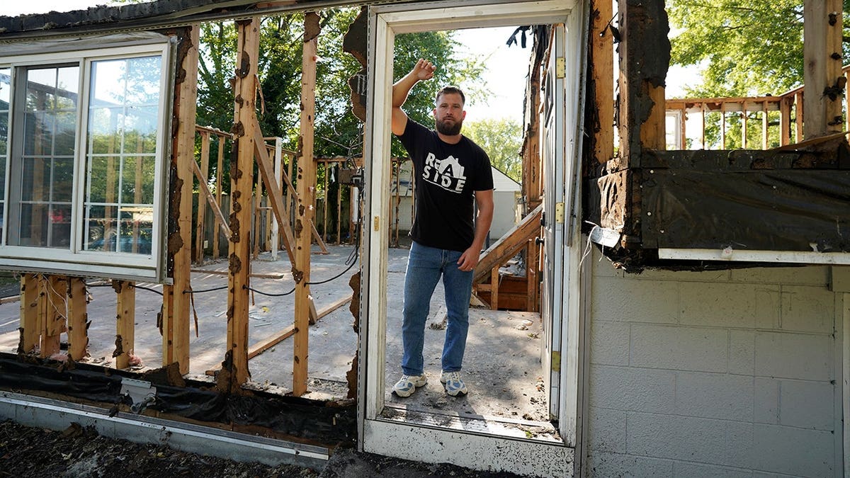 Tommy Harr stands in a doorway inside a stripped house frame.