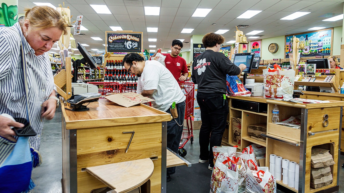 Trader Joe's employees work at the checkout counter with customers.