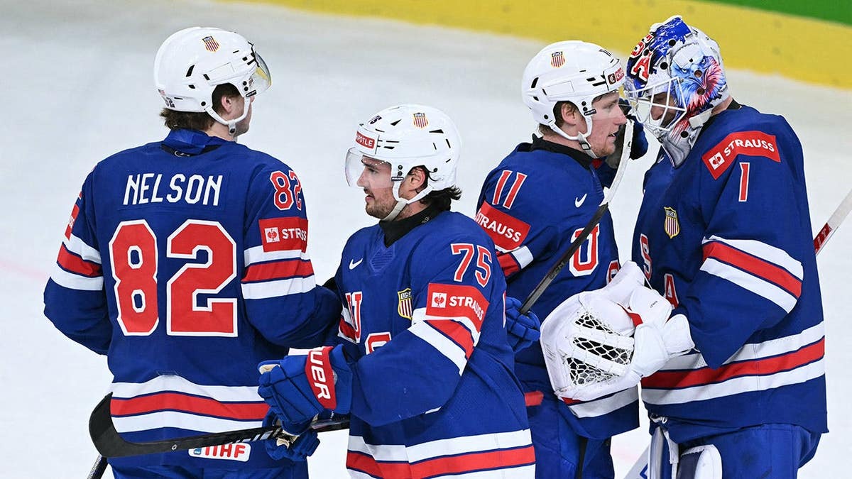 USA forwards Danny Nelson and Oliver Moore, defender Connor Clifton, and goalkeeper Devin Cooley celebrating on ice rink.