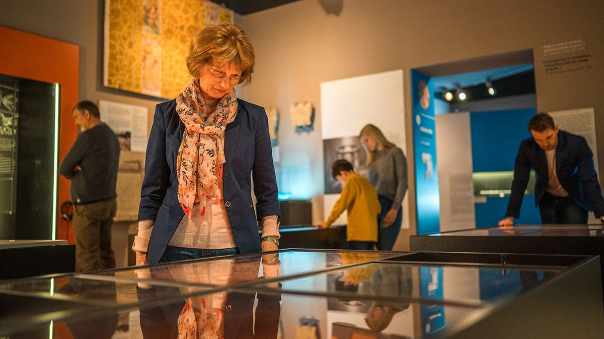 An elegant woman looking at museum display cases with people in background.