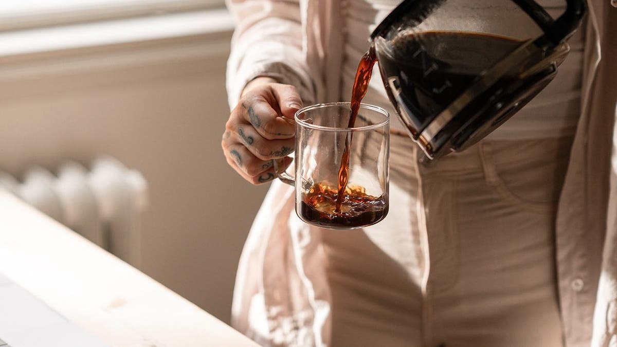 A woman pours coffee into a mug from a pot.