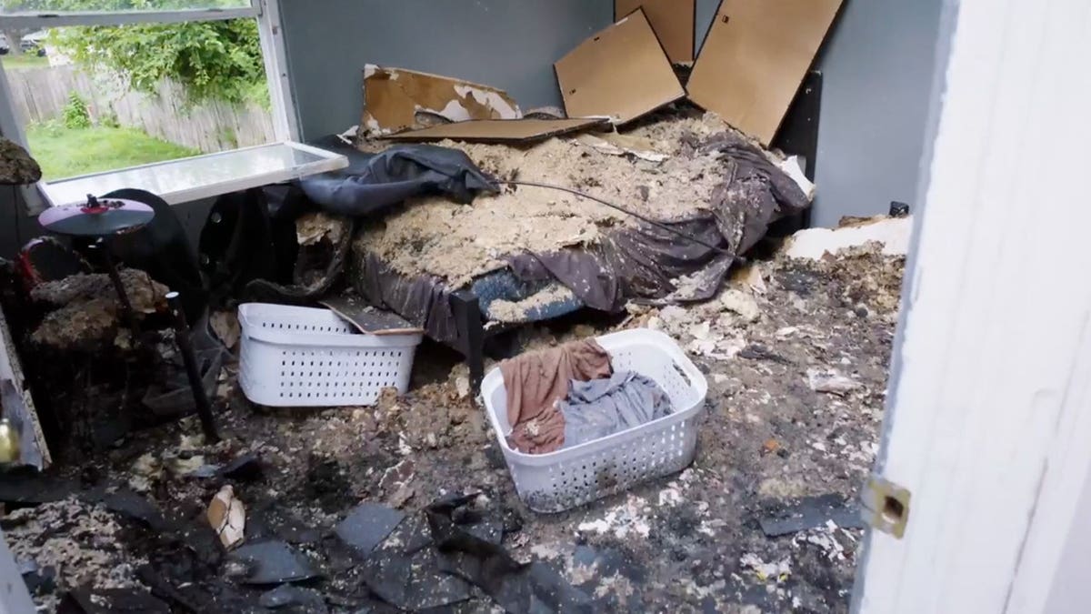 A damaged bedroom shows a bed covered in ash and debris.