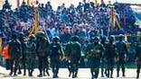 Multinational victims of scam centers stand in a crowd near an army