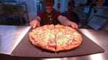 An employee placing a freshly cooked sliced pizza on a service counter inside a Pizza Hut restaurant.
