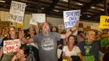 Protesters holding signs opposing a proposed AI data center project during a public meeting in Utah.