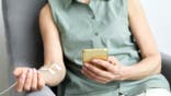 Unrecognizable woman receiving IV drip while using smartphone