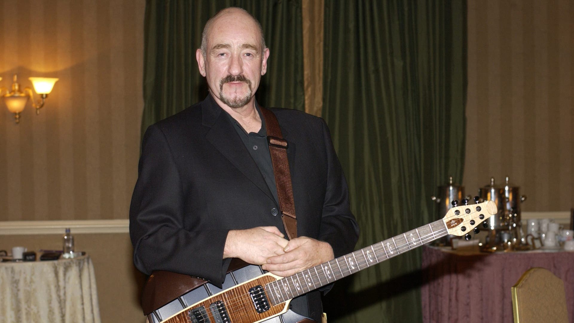 Dave Mason performs on stage with a guitar.