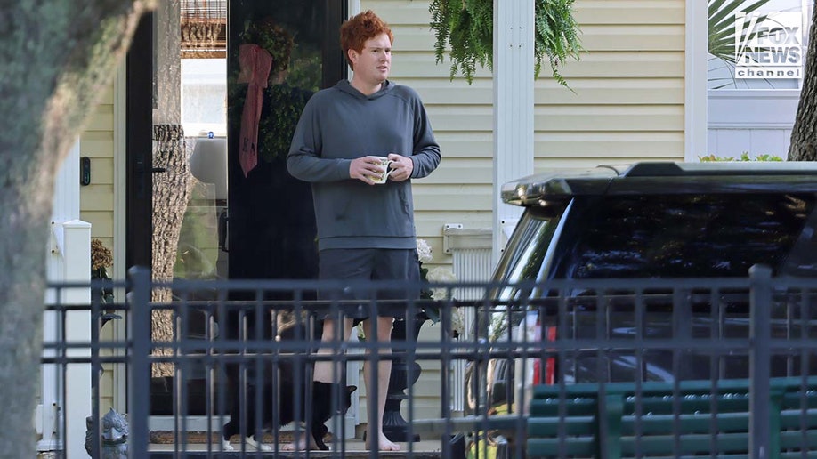 Buster Murdaugh sits on the front porch of a home while holding a coffee cup.