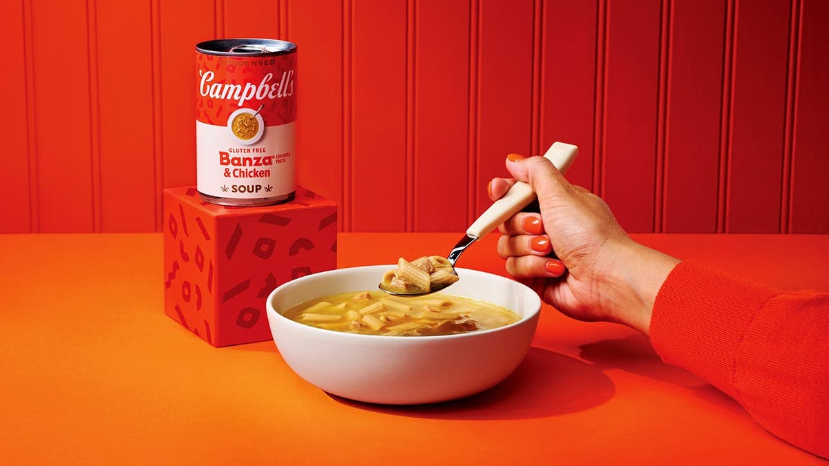 A woman holds a spoonful of Campbell's chicken noodle soup.