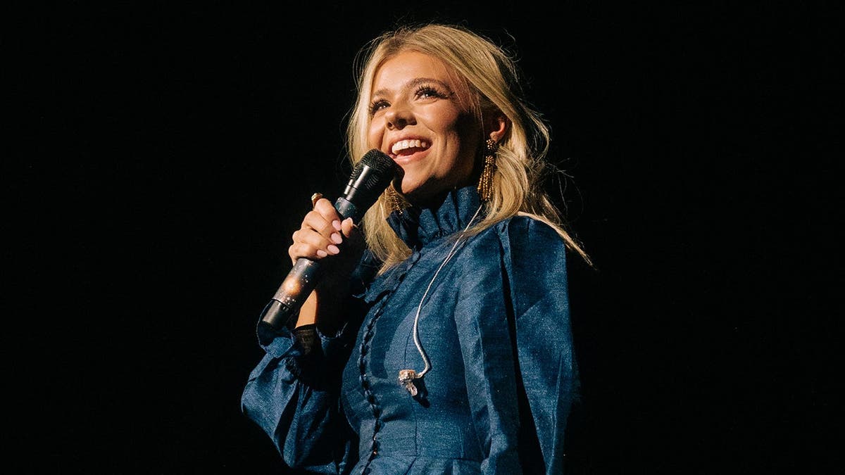 Anne Wilson usando um vestido jeans azul cantando no palco.