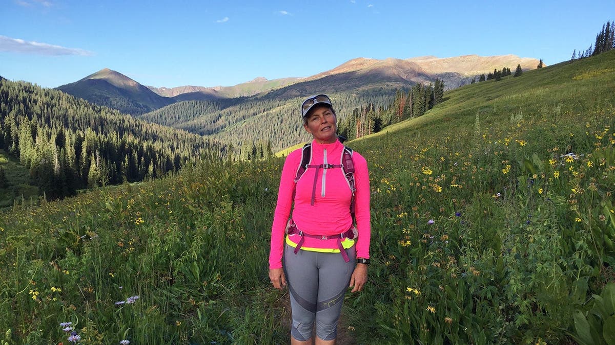 Kim Alexis in hiking gear against a mountain backdrop in the forest.