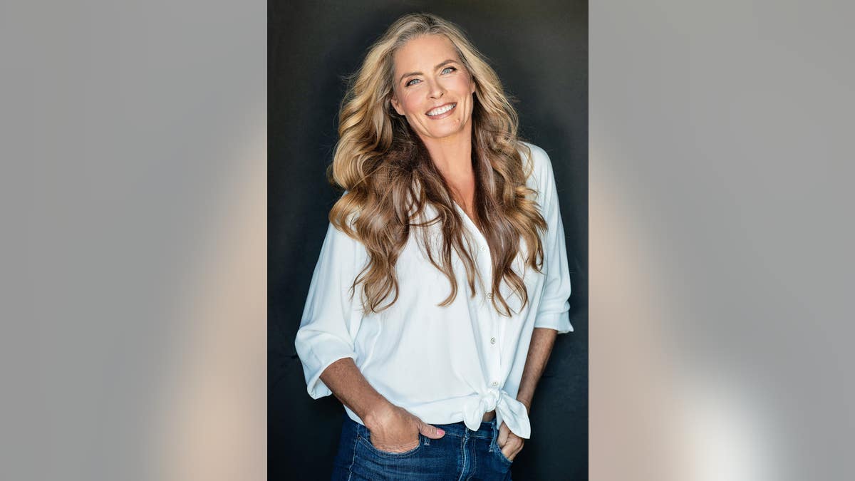 Kim Alexis smiling in jeans and a white oversized shirt.