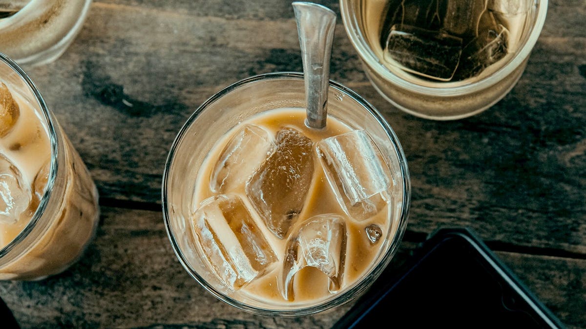 A spoon sits in a cup of coffee with ice cubes.