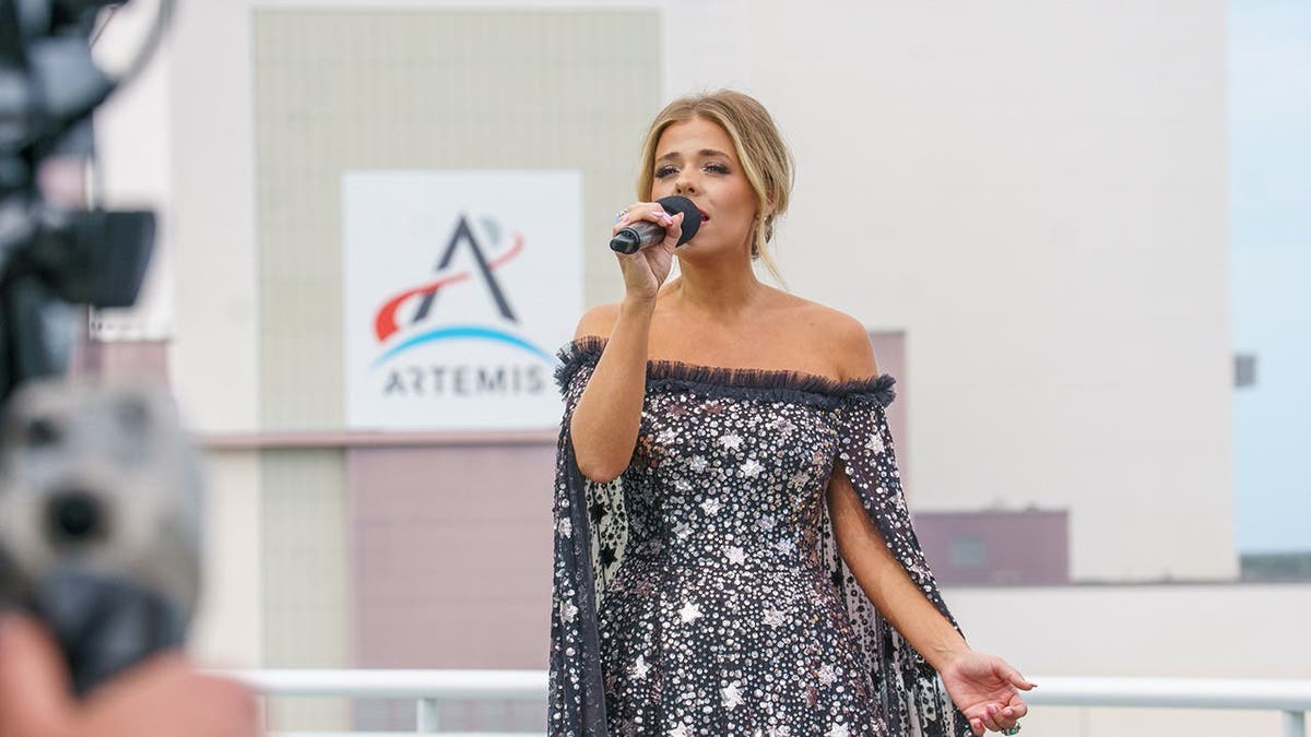 Anne Wilson usando um vestido preto e branco cantando para uma câmera que a filmava.