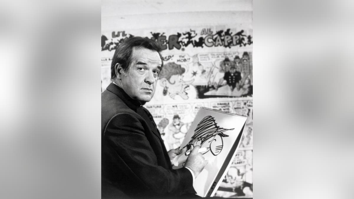 Al Capp standing and smiling in front of a backdrop.