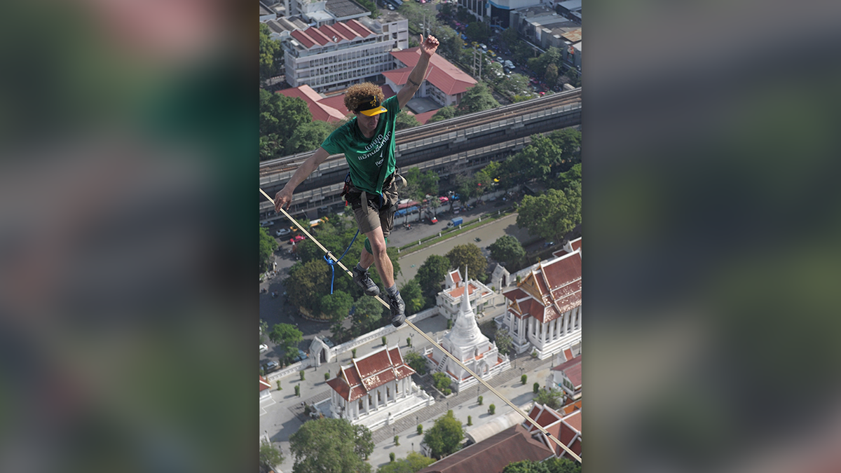 Daredevil Andy Lewis successful  a greenish  T-shirt and khaki shorts crosses a highline supra  Bangkok, Thailand