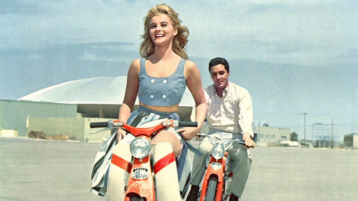 Ann-Margret and Elvis Presley riding scooters in a movie scene.