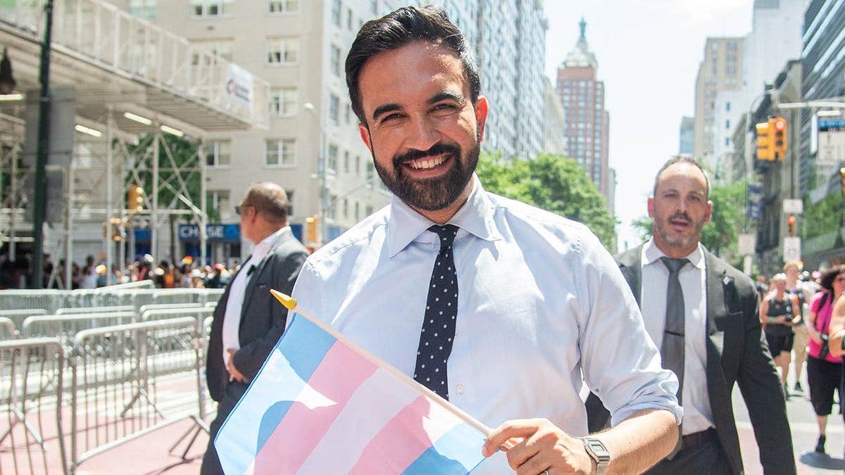 Zohran Mamdani smiles as he holds a transgender pride flag in 2025.
