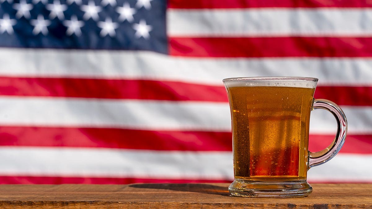 Copo de cerveja na mesa de madeira com bandeira americana ao fundo