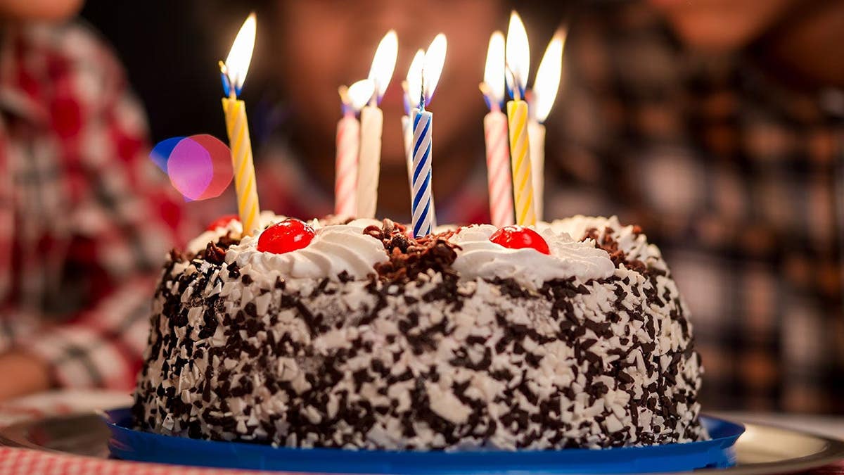 Small birthday cake with lit candles in front of children