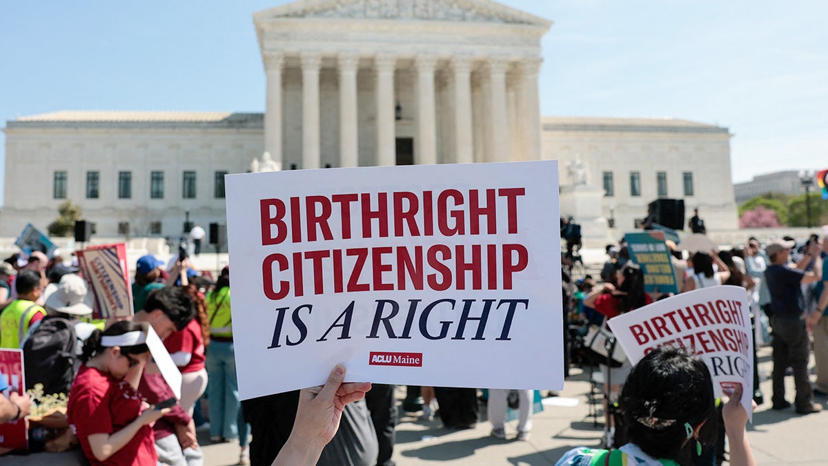 Demonstrators holding signs and rallying on the sidewalk outside the U.S. Supreme Court building.