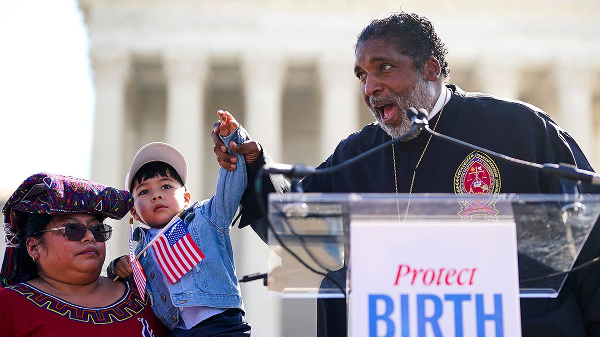 Rev. William Barber II speaking into microphones while standing outside the U.S. Supreme Court building.