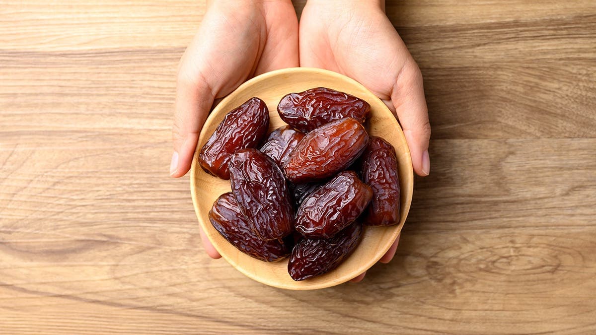A woman holds a bowl of dates.