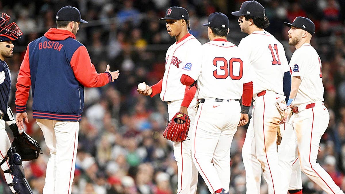 Brayan Bello entregando a bola para Chad Tracy no Fenway Park em Boston