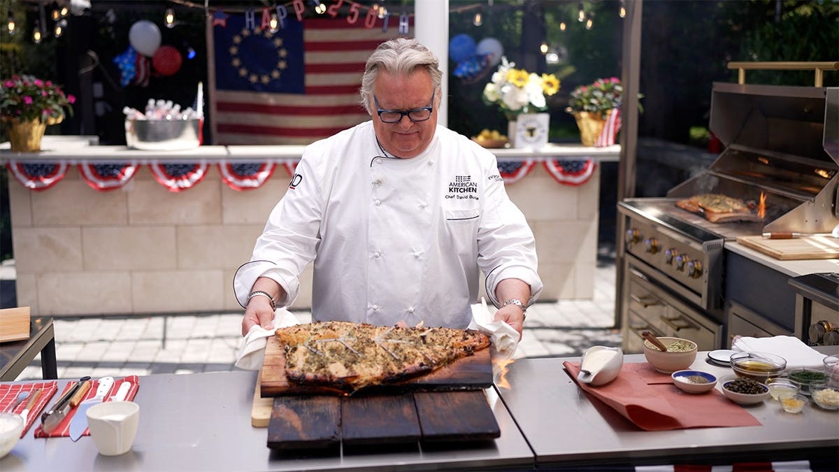 Chef David Burke prepares a cedar plank salmon before placing it on the grill during an outdoor cooking demonstration.