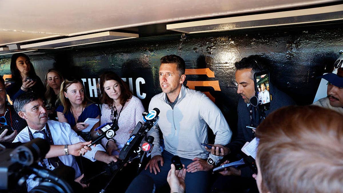 Buster Posey speaking at a microphone at Oracle Park in San Francisco