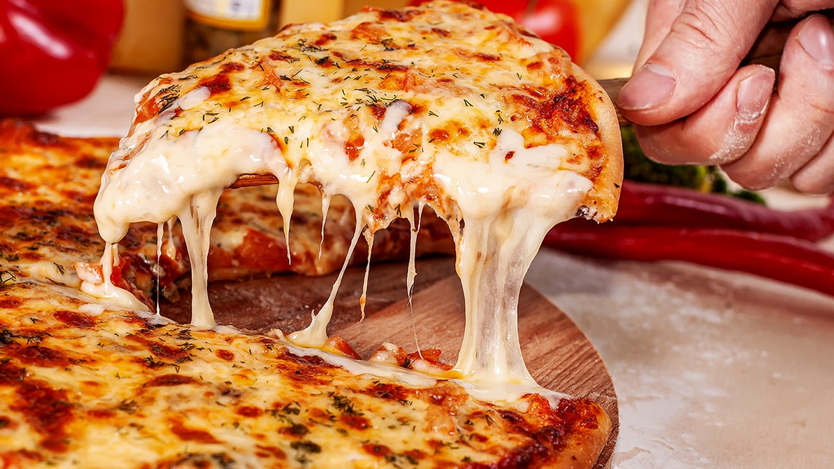 A hand holds a slice of cheese pizza with a spatula.