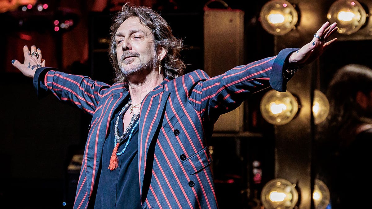 Chris Robinson holds his arms out on stage