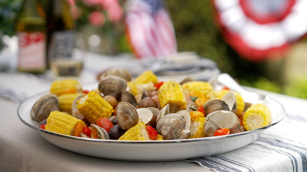 A traditional New England-style clam bake dish featuring clams, lobster, corn on the cob, potatoes, and sausage.