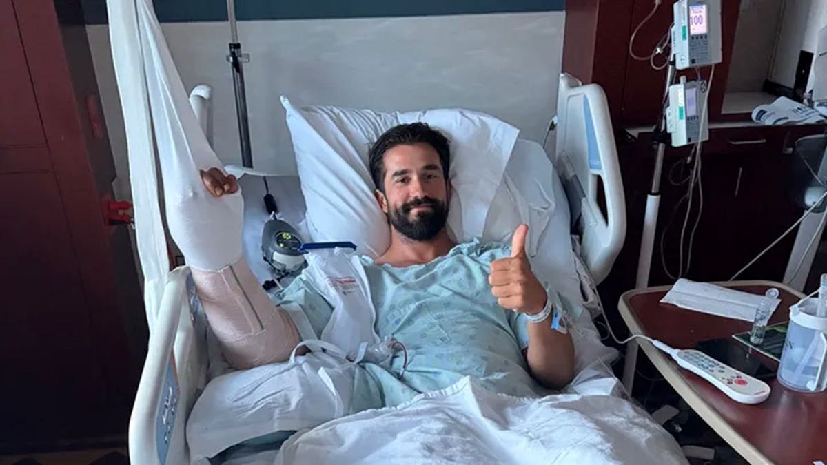 Daniel Crago laying in a hospital bed with his thumb up.