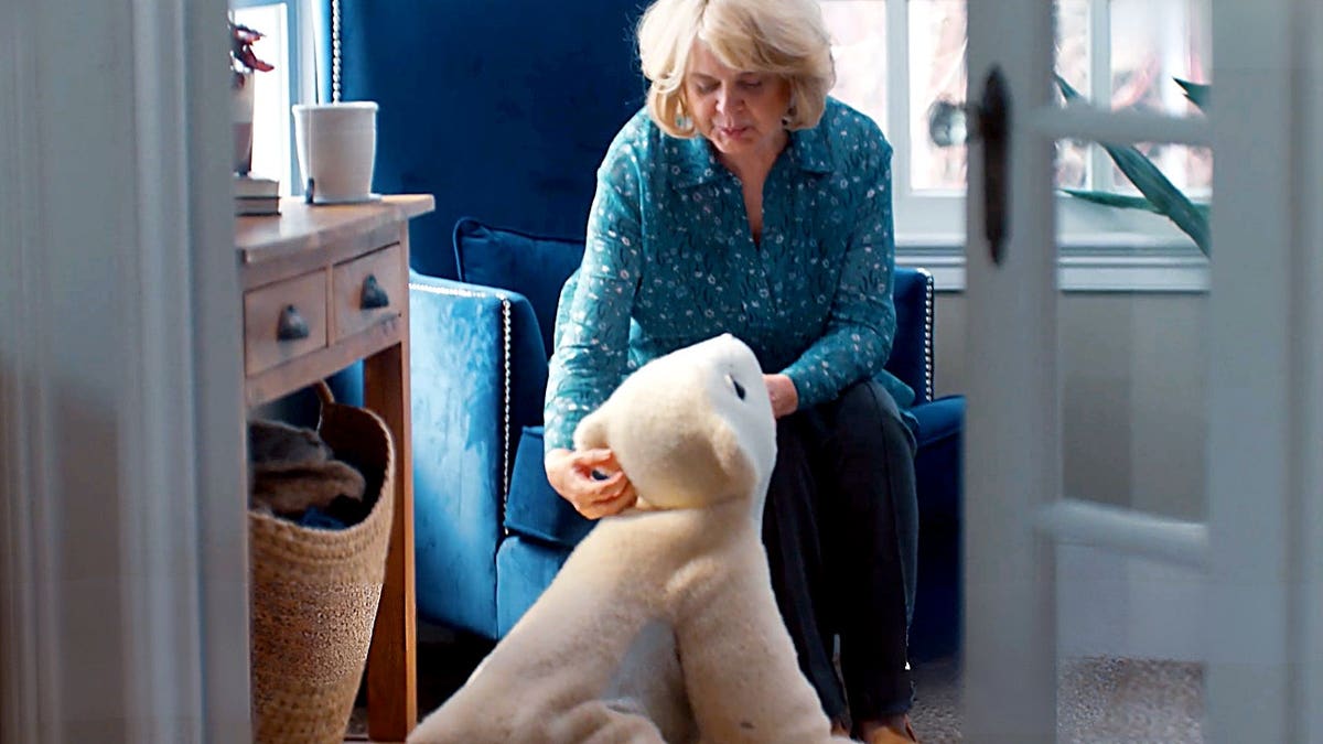 An elderly woman pets a robot pet.