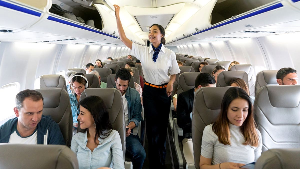 Happy flight attendant walking aisle closing overhead compartments inside airplane cabin