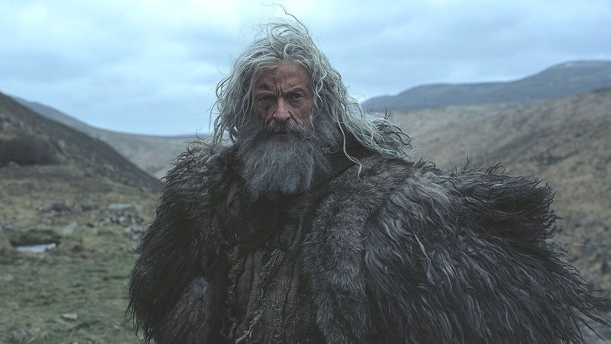 Hugh Jackman in a fur cloak standing in a mountain valley for