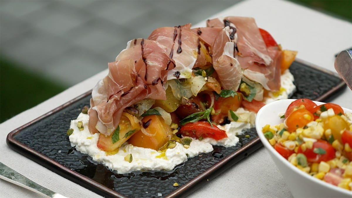 An heirloom tomato and beet salad topped with prosciutto and arranged on a serving plate.