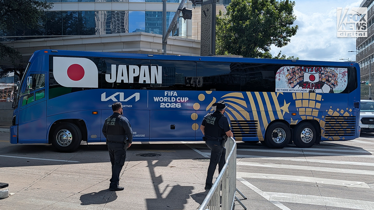 A bluish FIFA World Cup 2026 squad autobus displaying Japan's sanction and emblem is parked connected a metropolis thoroughfare arsenic constabulary officers guidelines nearby.