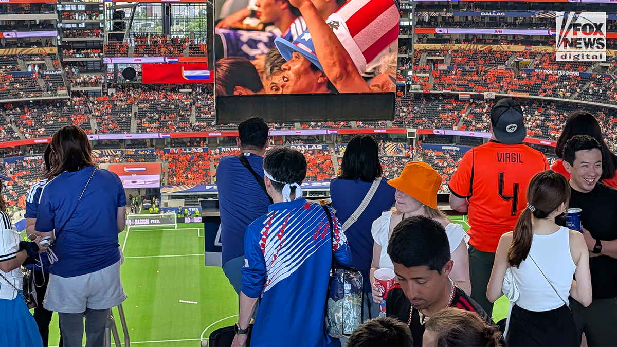 Fans wearing Japan and Netherlands squad apparel watch nan section from a stadium suite during a FIFA World Cup match, pinch a ample video committee visible supra nan stands.